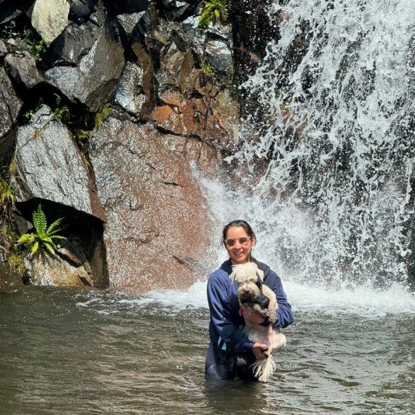 Mujer feliz cargando a su perro blando dentro de una cascada